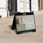A black, small A-frame with a QR code for a pottery class, displayed outdoors.