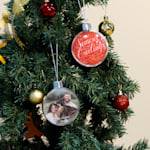 Two Christmas baubles hanging from a tree, with one featuring a typographic design and one featuring a family photo.