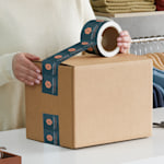 A woman in a white sweater applying white plastic Self-adhesive packaging tape to a cardboard box. The tape is custom printed with a design for a clothing and fashion business.