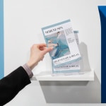 A person takes a saddle-stitch booklet for a spa from a booklet holder.