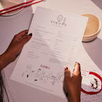 A diner holding a menu for a Chinese restaurant, just above their place setting.