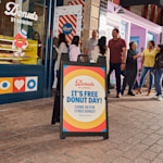 A black Signicade® featuring “free donut day” messaging in front of a donut shop.