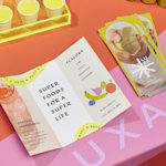 Tri-fold brochures for a health supplements brand, displayed on a colorful table, with samples in the background.