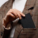 A person putting a kraft business card holder in their jacket pocket.