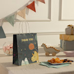 A party bag perched on a birthday tablescape, printed with a colorful dino motif.   
