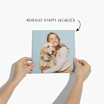 A pair of hands holding a photo tile printed with a picture of a woman embracing a Golden Retriever.