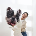 A woman showing her dog a pet face pillow featuring the dog’s face.