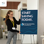 A woman standing next to a financial banking foam board displayed on an easel, with a 24-hour delivery icon in the corner.
