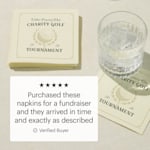 Napkins personalized for a charity golf tournament stacked next to a glass of water. 