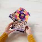 Una persona sujetando un menú díptico de una tienda de chocolates, con un conjunto de menús dípticos en el fondo.