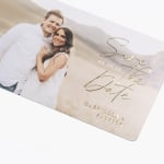 Una tarjeta Save the Date personalizada con una foto de una pareja y detalles en relieves metalizados.