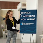 Una mujer de pie junto a un cartel de cartón pluma que se muestra sobre un caballete.