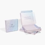 3 cajas postales cuadradas, dos están colocadas de manera plana y la tercera está parada sobre un extremo. La caja plana superior está abierta mostrando el mensaje que lleva adentro.