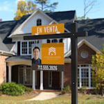 Un poste colonial negro con un cartel para inmobiliarias y una placa de información de “se vende” colocado frente a una casa.