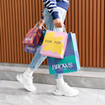 Una persona cargando muchas bolsas de papel estándar de varios tamaños y colores y con diferentes marcas.