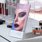 Se muestran tarjetas informativas con efecto metálico resplandeciente morado de un maquillista, colocadas en el mostrador de un salón de belleza.