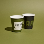2 vasos de papel desechables personalizados sobre una mesa, junto a una bolsa de papel.