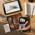 Un portafolio de arquitectura se muestra junto a una tableta con un diseño en 3D y planos enrollados sobre un escritorio de madera.