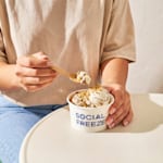 2 vasos de papel con logotipos, con helado de pistacho y de chocolate y con galletas encima.