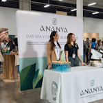 2 mujeres de pie frente a un backing publicitario de tubo de un day spa en una feria comercial.