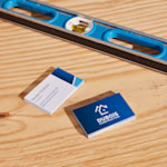 Piles de cartes de visite express 24h pour une entreprise de construction posées sur un comptoir en bois, à côté d’un niveau à bulle.