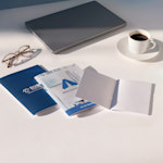 Carnets personnalisés avec des logos d’entreprise sur un bureau blanc à côté d’un ordinateur portable, de lunettes et d’une tasse à café.