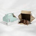 Deux boîtes à pignon personnalisées créées pour un fabricant de produits de beauté. Une boîte à pignon est couchée sur le flanc; elle contient du papier plissé et deux flacons de produit.