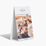 Panneau sur pieds en carton ondulé faisant la publicité d’un salon de coiffure, avec un code QR pour aider les clients à prendre rendez-vous.