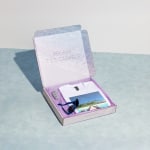 Une boîte carrée pour envoi postal remplie d’articles publicitaires pour une agence de voyages.