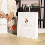 Une employée remplit des sacs en papier kraft blanc avec les articles d’une entreprise de céramique artisanale.