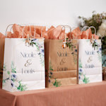 Trois sacs de fête d’un mariage dotées de motifs floraux et remplis de papier de soie couleur saumon.
