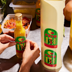 Une personne en train de détacher des étiquettes en forme d’arc d’un rouleau simple et de les appliquer sur des bouteilles de sauce piquante.