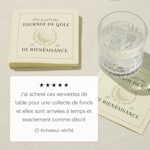 Une pile de serviettes de table personnalisées pour un tournoi de golf caritatif à côté d’un verre d’eau. 