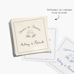 Une pile de serviettes de cocktail blanches et écru personnalisées pour un mariage, avec une note indiquant l’option de couleurs blanc et écru. 