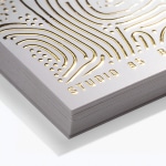 Et nærbilde av en bunke visittkort med hevet gullfolie og rette hjørner.