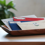 Stapel enveloppen in verschillende kleuren in een postvak op een houten tafel.