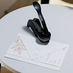 Een reliëfstempel ligt op een witte tafel naast een gesloten envelop met bloemenontwerp.