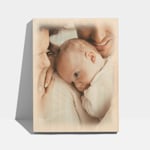 Een houten fotoblok met een foto van een stel dat hun pasgeboren baby vasthoudt.