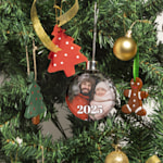 Uma bola de Natal pendurada numa árvore de Natal, personalizada com a imagem de um pai e da sua filha vestidos com roupas de inverno.