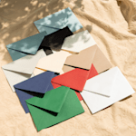 Vários envelopes coloridos dispostos sobre uma toalha de mesa texturizada de cor creme.