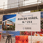 Uma lona de uma empresa de construção presa à vedação de um estaleiro de construção, com informações sobre o novo edifício.