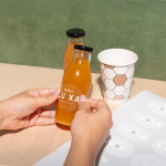 A clear sticker promoting a wellness brand being applied onto a juice bottle