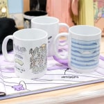 Three white mugs featuring artwork by @artofbrentos